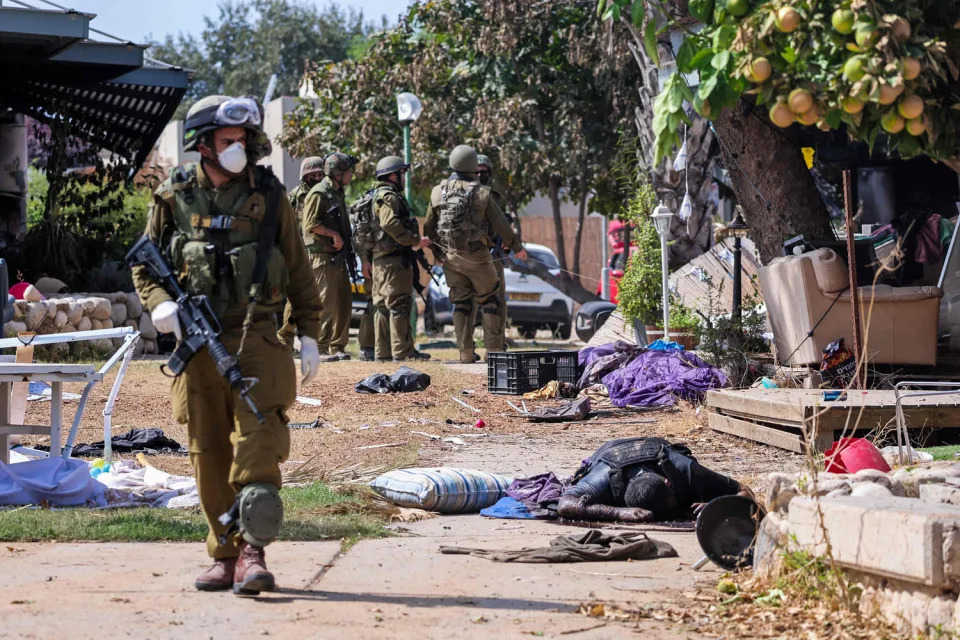 Israeli soldiers stand near the body of a Palestinian militant in Kfar Aza, Israel (Thomas Coex / AFP - Getty Images)