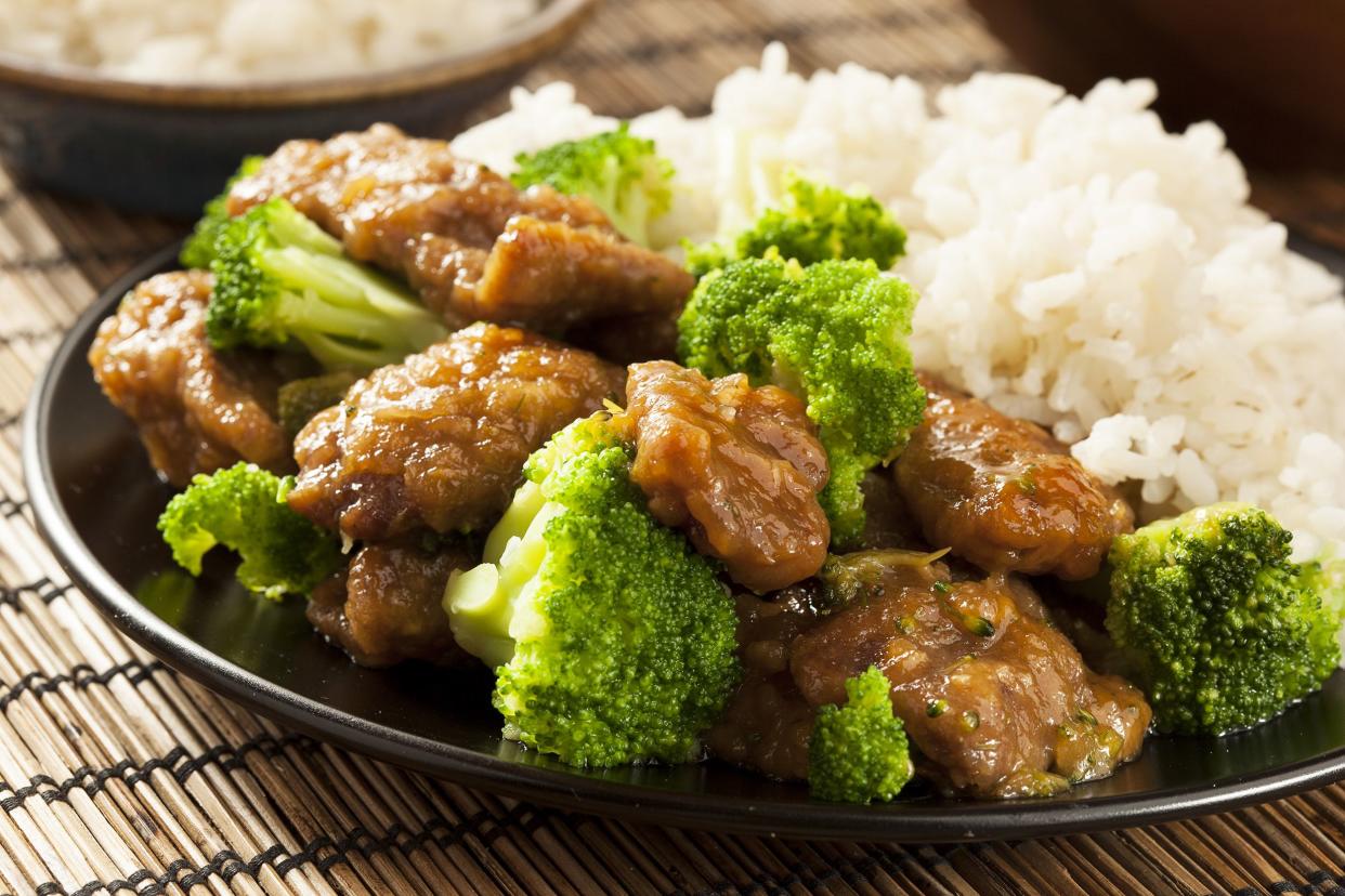 Closeup of the best easy beef and broccoli stir-fry with separate rice on a black plate on a bamboo table mat with another bowl of rice blurred in the background