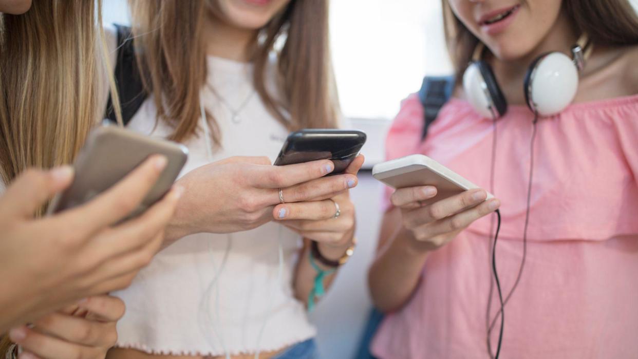 Three teenage girls huddled around using mobile phones