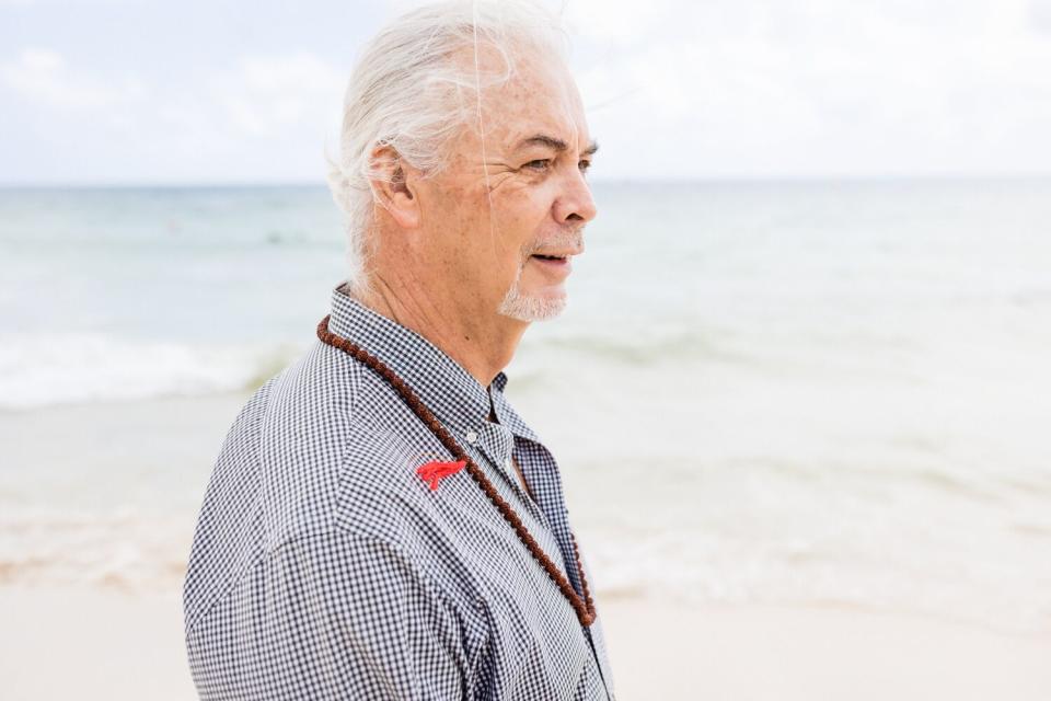 A man in three-quarter profile walking along a coastline