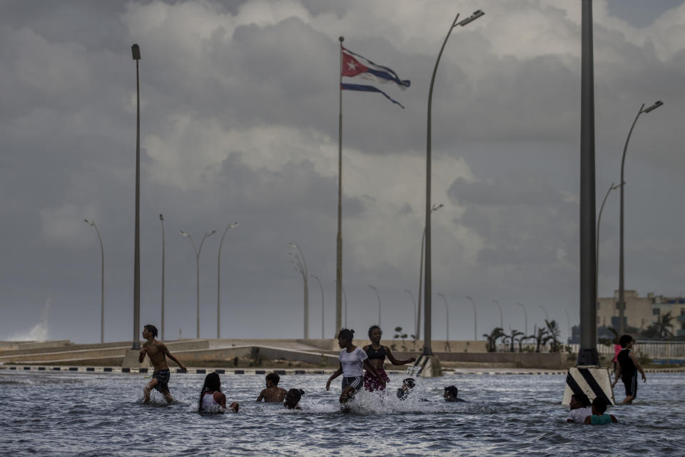 FILE - A Cuban flag, shredded by the winds of Hurricane Ian, flies in the air while children play in the seawater from the waves breaking on Malecon in Havana, Cuba, Sept. 29, 2022. When Category 3 hurricane Ian ravaged western Cuba at the end of September, Cuba was already in one of its worst economic, political and energy crises in decades, thanks to the coronavirus pandemic and the Russian war with Ukraine, among other factors. (AP Photo/Ramon Espinosa, File)