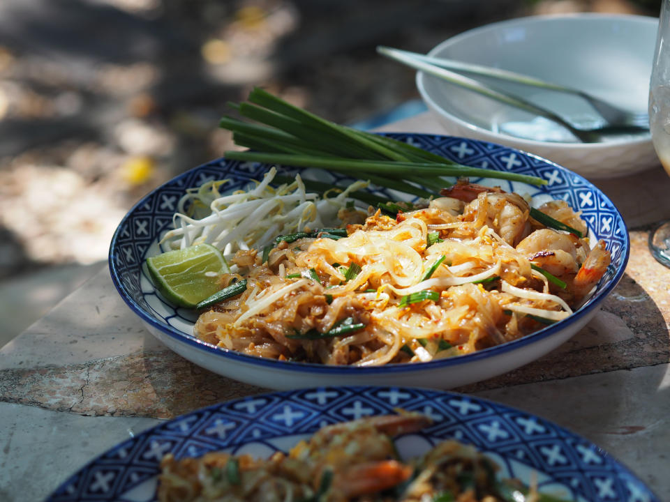 Thin flat noodles stir fried with egg and tofu in blue and white bowl with lime wedge on the side.