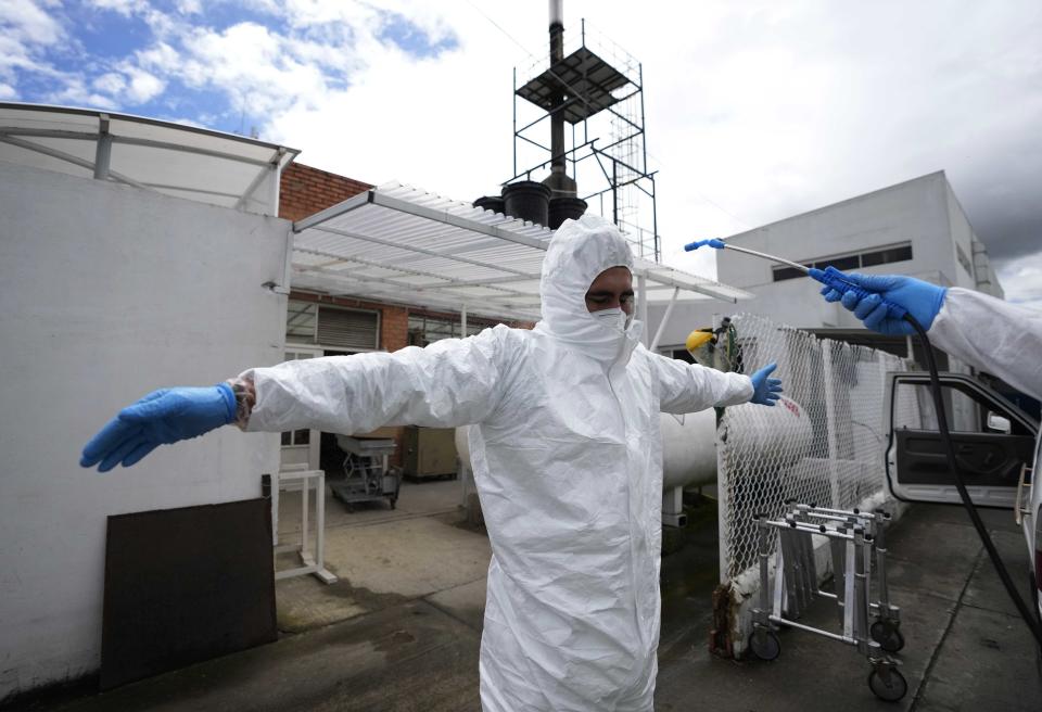 A funeral worker spreads out his arms as he is disinfected after handling the remains of a person who died from the new coronavirus, outside the crematorium at the Zipaquira's Park Cemetery in Zipaquira, Colombia, Friday, June 18, 2021. Funeral workers in Colombia are struggling to dispose of bodies as the country experiences a surge in deaths from COVID-19. (AP Photo/Fernando Vergara)