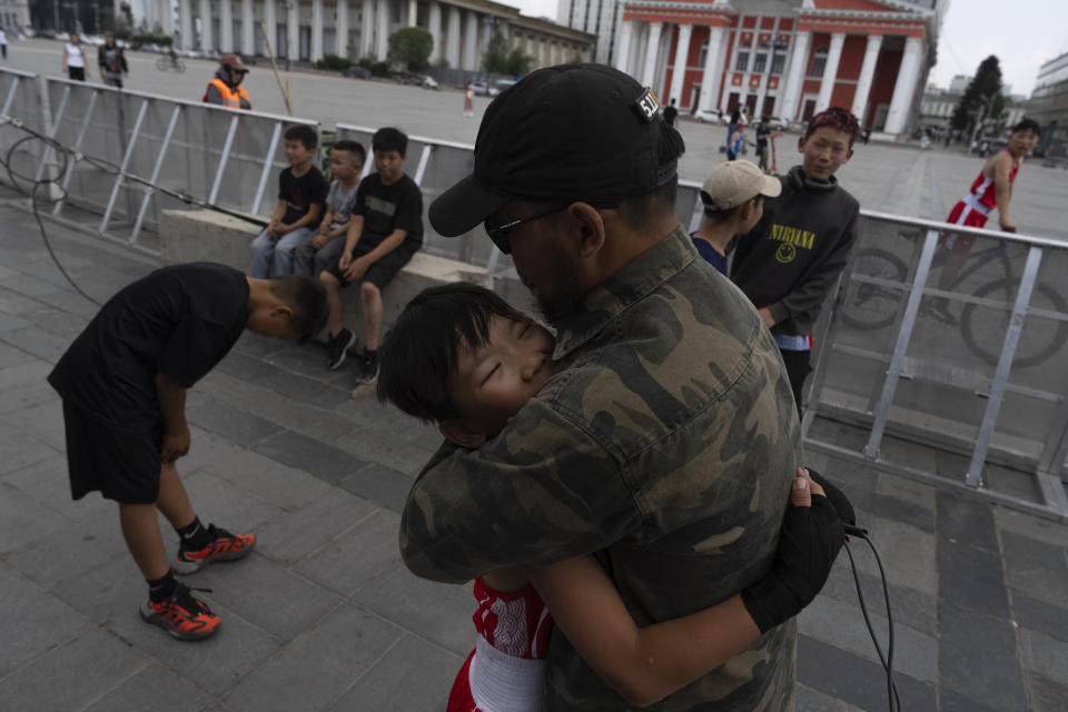 Kherlen Nasantogtokh hugs his twelve-year-old son Gerelt-Od Kherlen after his winning a bronze medal boxing match on Sukhbaatar Square in Ulaanbaatar, Mongolia, Tuesday, July 2, 2024. Growing up in a Ger district without proper running water, Gerelt-Od fetched water from a nearby kiosk every day for his family. Carrying water and playing ball with his siblings and other children made him strong and resilient. (AP Photo/Ng Han Guan)