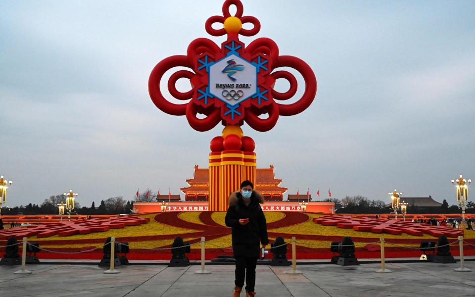 A man walks past an installation displaying a Chinese knot with the logo of the Beijing 2022 Winter Olympics at Tiananmen Square in Beijing - JADE GAO/AFP via Getty Images