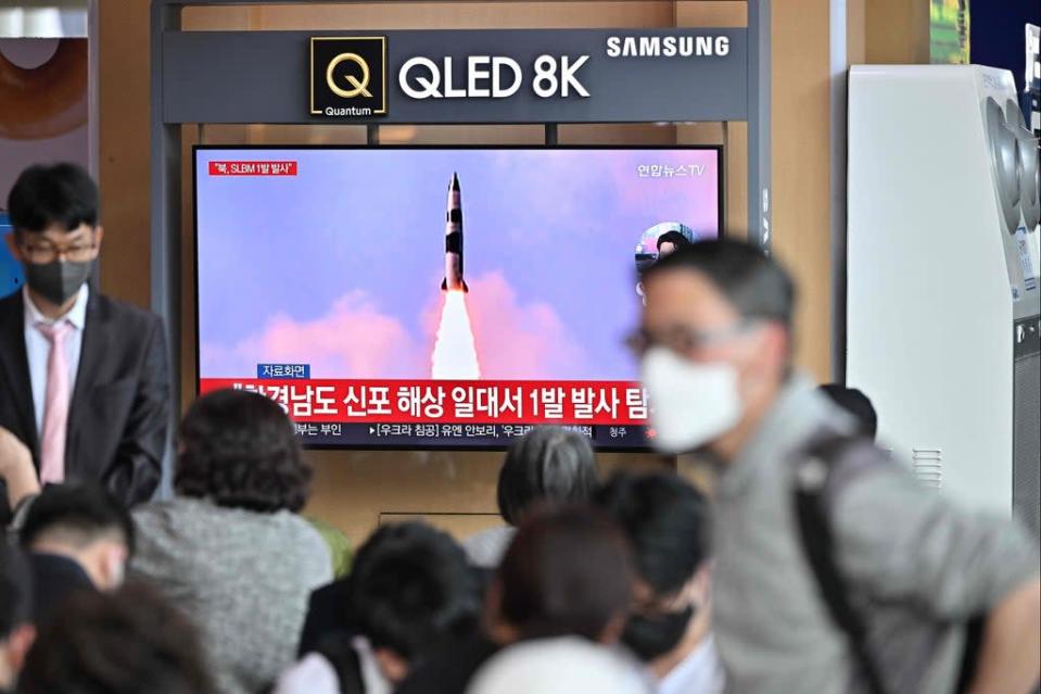 People watch a television screen showing a news broadcast with file footage of a North Korean missile test (AFP via Getty Images)