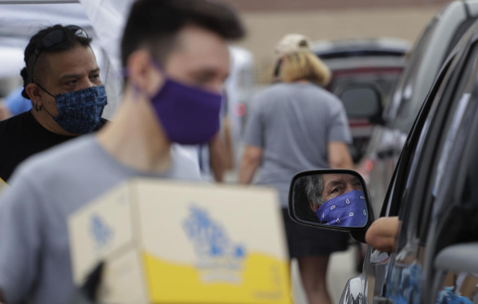 A driver wearing a bandana as protection is reflected in a mirror as volunteers help the San Antonio Food Bank distribute food to more that 2,000 at the Alamodome in San Antonio, Friday, April 17, 2020. San Antonio remains under stay-at-home orders due to the COVID-19 outbreak. (AP Photo/Eric Gay)