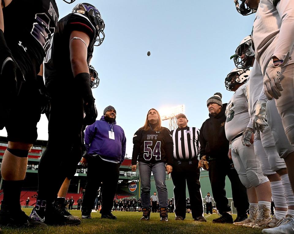 Wearing her son Tony Pena's old jersey number, Lena Laferriere of Grafton, center, performs the opening coin toss with her husband, Bryan Pena, left, before Blackstone Valley Tech's Thanksgiving Eve game against Nipmuc at Fenway Park, Nov. 24, 2021. Former Blackstone Valley Tech football player Tony Pena lost his battle with brain cancer in January 2020 and the team's seniors dedicated their season to his memory.