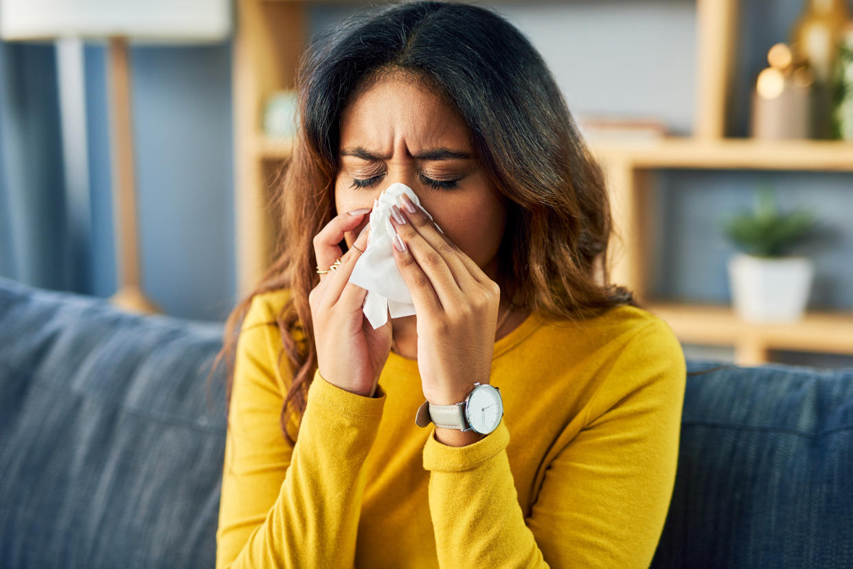 Shot of a young woman blowing her nose while sitting at home