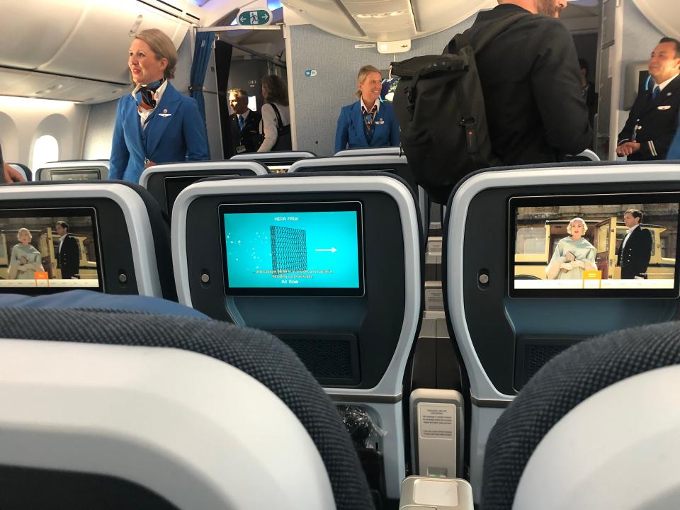 An overview of the new KLM Premium Comfort cabin from behind. A small sign noting that lavatories are located to the rear of the cabin is visible above the flight attendant near the forward bulkhead.