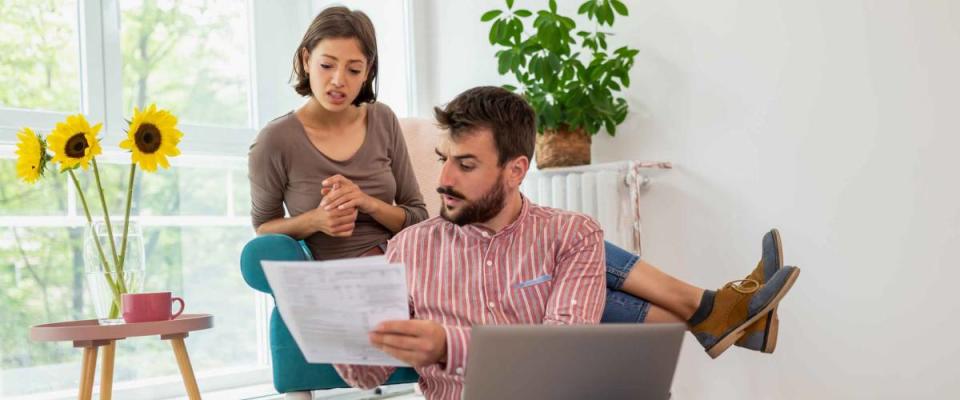 Young couple sitting in living room together, looking at document and looking serious