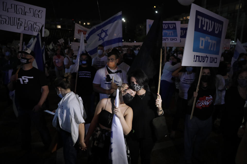Israelis wear face masks wave placards and Israel's national flags during a rally marking 25 years since the assassination of the late Israeli Prime Minister Yitzhak Rabin, at Rabin Square, in Tel Aviv, Israel, Saturday, Nov. 7, 2020. (AP Photo/Sebastian Scheiner)