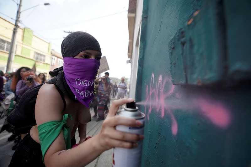 A woman sprays paint on a wall during a march to mark International Women's Day in Bogota