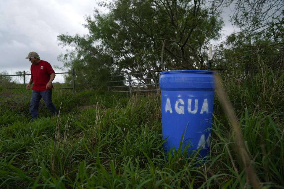 Migrant rights activist Eduardo Canales walks behind one of his blue water drops Saturday, May 15, 2021, in Falfurrias, Texas. Every week, Canales fills up blue water drums that are spread throughout a vast valley of Texas ranchlands and brush. They are there for migrants who venture into the rough terrain to avoid being caught and sent back to Mexico. (AP Photo/Gregory Bull)