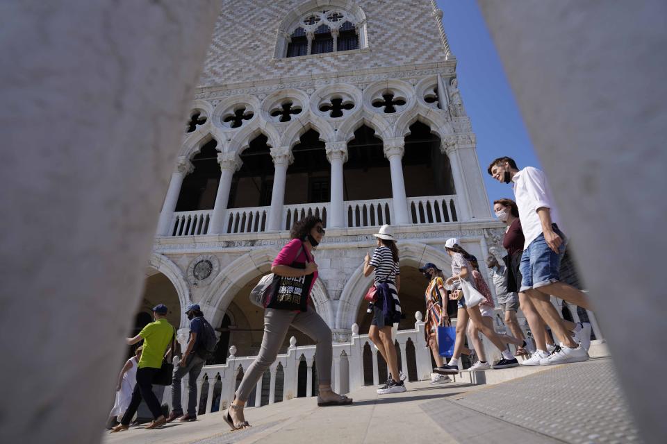 Tourists walks on a bridge in front of Palazzo Ducale, in Venice, Italy, Thursday, June 17, 2021. After a 15-month pause in mass international travel, Venetians are contemplating how to welcome visitors back to the picture-postcard canals and Byzantine backdrops without suffering the indignities of crowds clogging its narrow alleyways, day-trippers perched on stoops to imbibe a panino and hordes of selfie-takers straining for a spot on the Rialto Bridge or in front of St. Mark's Basilica. (AP Photo/Luca Bruno)