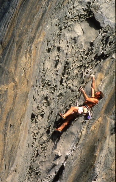Man climbs overhanging yellowed rock filled with pockets.