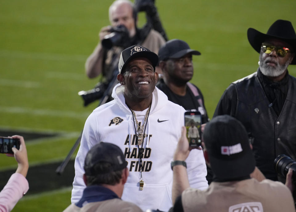 Colorado head coach Deion Sanders, center, stops and pulls off his sunglasses and smiles for the crowd as players warm up before an NCAA college football game against Colorado State, Saturday, Sept. 16, 2023, in Boulder, Colo. (AP Photo/David Zalubowski)