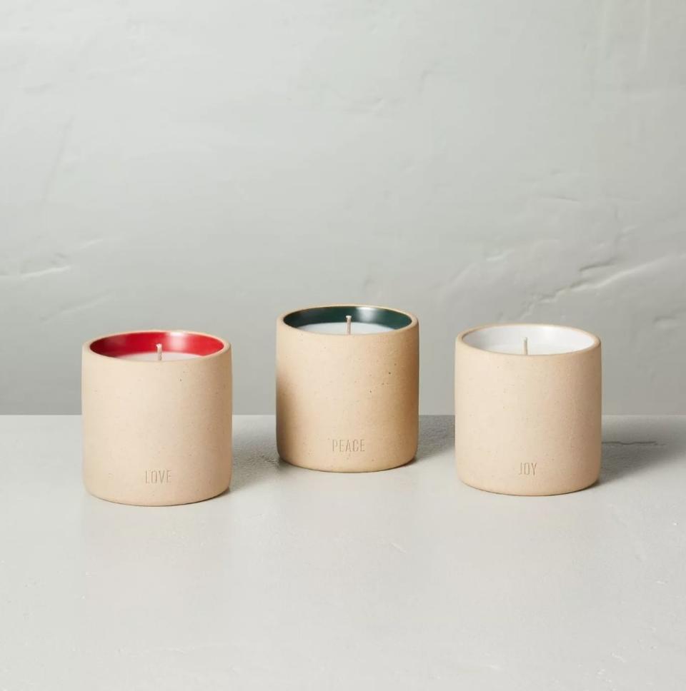 Three beige jarred candles that say "love," "peace," and "joy" on the bottoms