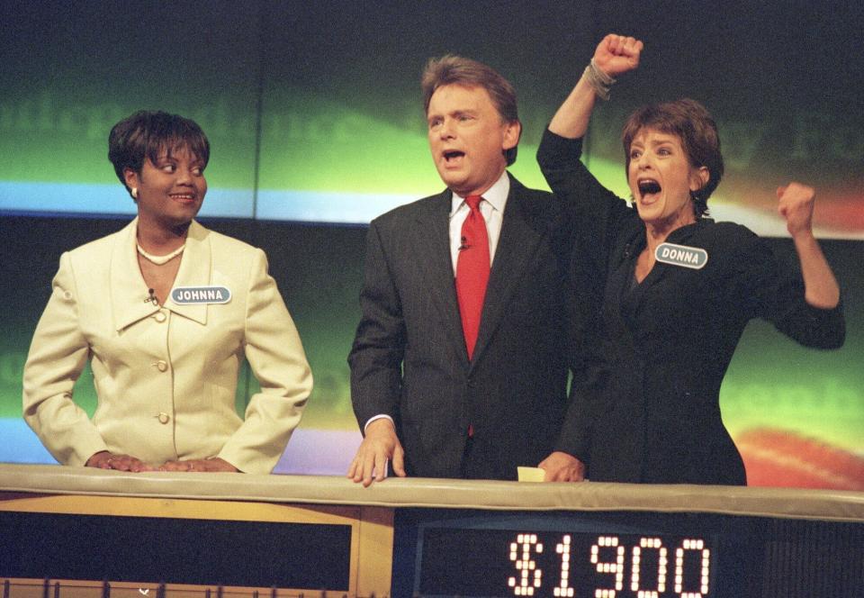 FILE - Johnna Goodwin, left, watches as Donna Handel, right, reacts after winning on "Wheel of Fortune," with host Pat Sajak during a taping of the game show in Philadelphia on April 17, 1999. The game show was in Philadelphia for the weekend taping a week's worth of shows. Ryan Seacrest will replace the retiring Sajak as host of “Wheel of Fortune.” (AP Photo/William Thomas Cain, File)