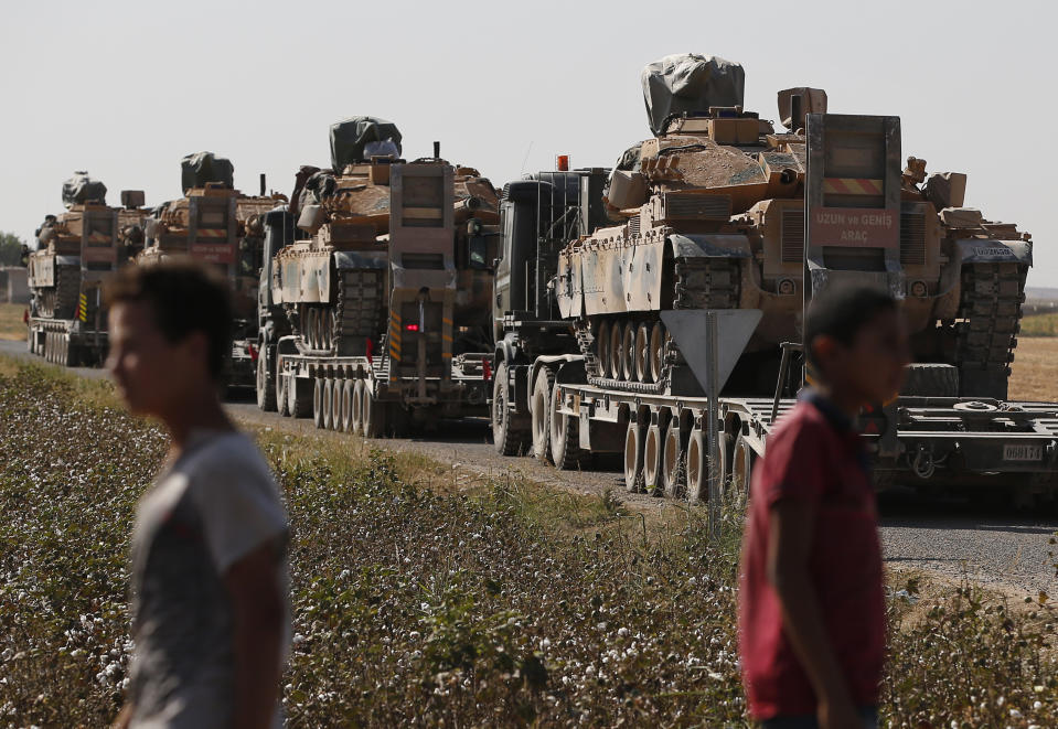 Local residents look on as a convoy of Turkish forces' trucks transporting tanks is driven on a road towards the border with Syria in Sanliurfa province, Saturday, Oct. 12, 2019. Turkey's military said it captured a key Syrian border town under heavy bombardment Saturday as its offensive against Kurdish fighters pressed into its fourth day with little sign of relenting despite mounting international criticism. (AP Photo/Lefteris Pitarakis)