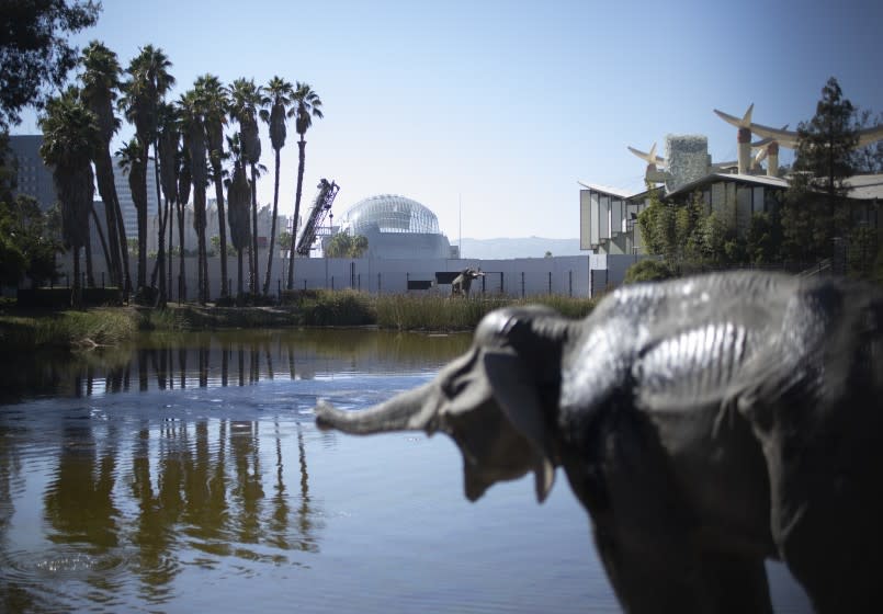 The spherical form of the Geffen Theater is seen in the distance, beyond the Lake Pit and a sculpture of a baby mammoth