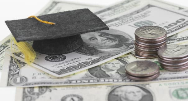 Mortarboard and US dollar banknotes and stack of quarters close up