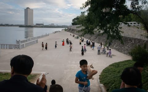 A boy carries a dog up a flight of steps before a group of recreational dancers beside the Taedong river in Pyongyang - Credit: AFP