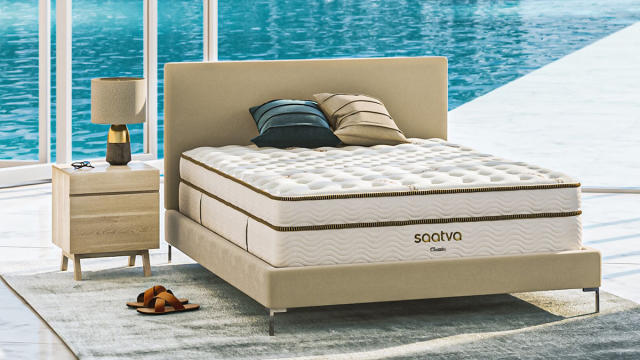 Best mattress: the Saatva Classic luxury innerspring hybrid mattress placed on a faux leather bed frame overlooking a bright blue swimming pool