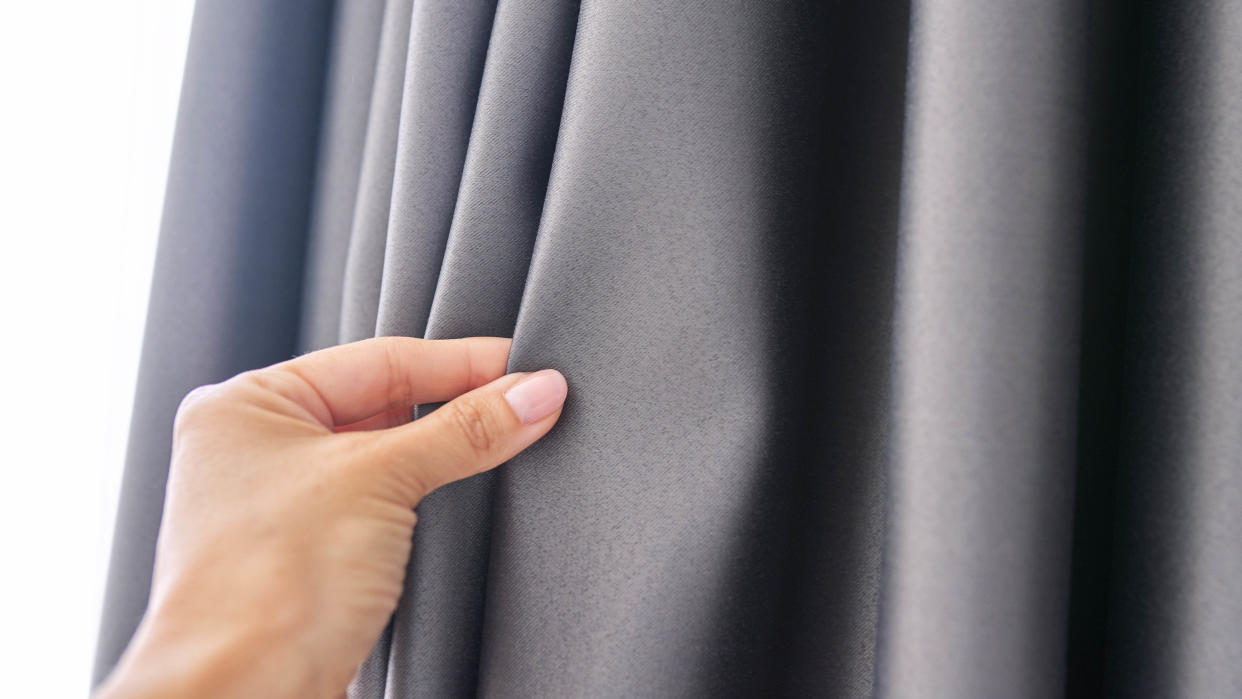  A hand pinching blackout curtains 