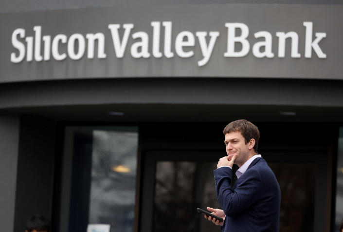 A customer in suit and starched shirt, looking stumped and holding his cellphone, stands outside a Silicon Valley Bank.