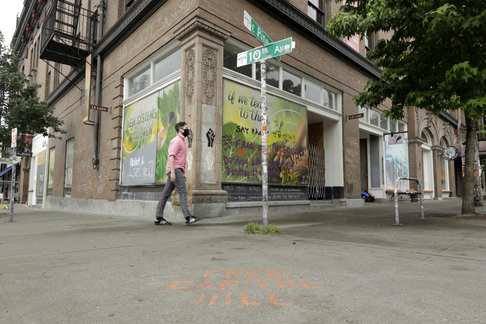 A pedestrian walks past the Oddfellows Hall, Saturday, June 20, 2020, at the intersection of 10th Ave. and Pine St. next to a barricade for the Capitol Hill Occupied Protest zone in Seattle. A pre-dawn shooting near the area left one person dead and critically injured another person, authorities said Saturday. The area has been occupied by protesters after Seattle Police pulled back from several blocks of the city's Capitol Hill neighborhood near the Police Department's East Precinct building. (AP Photo/Ted S. Warren)