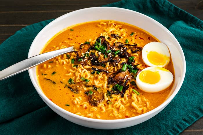 Bowl of noodle soup with mushrooms, soft-boiled egg halves, and garnish, served with a spoon on a cloth napkin