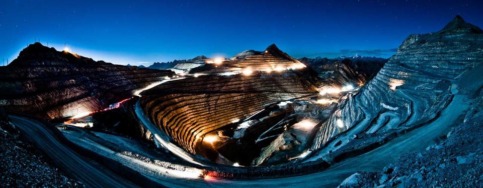 Open pit mine at night, with lights on and mountains surrounding.