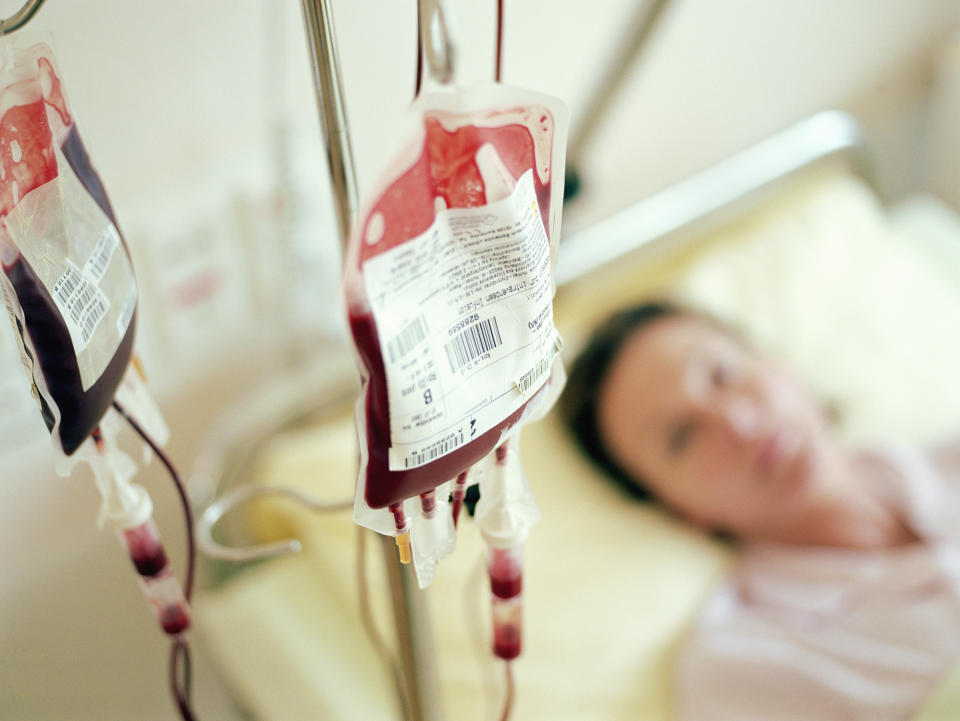 Blood bags hanging on IV stands next to a blurred person lying in a hospital bed