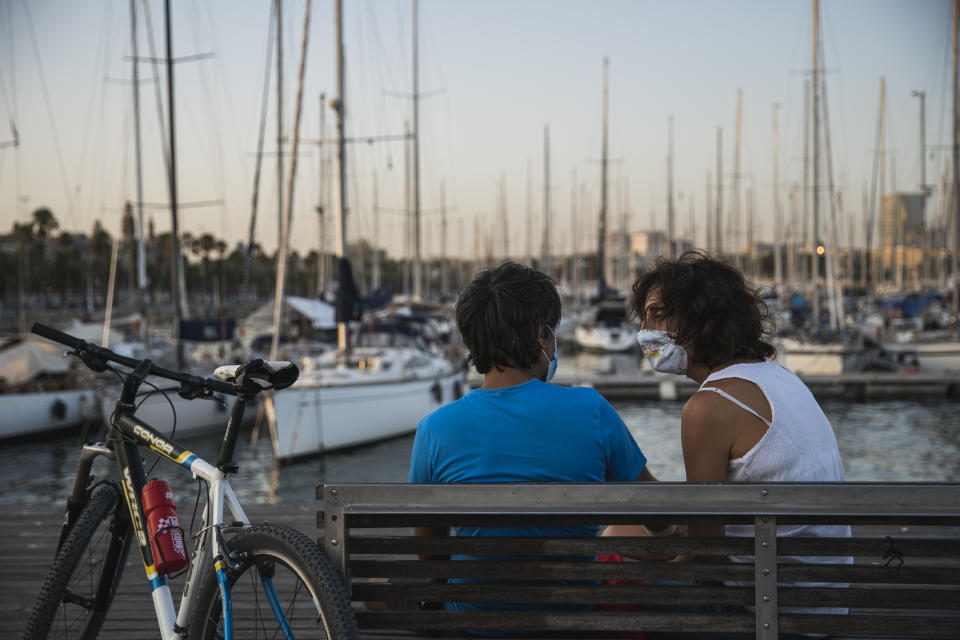 BARCELONA, SPAIN - JULY 27: People, wearing protective face masks, sit on a bench at Port Vell on July 27, 2020 in Barcelona, Spain. Spanish officials insisted it was still safe to travel to the country despite a recent rise in coronavirus (COVID-19) cases, which led the UK government to reimpose a 14-day quarantine on arrivals from Spain. The Catalonian government had recently issued a stay-at-home recommendation that included the regional capital, Barcelona. (Photo by Cesc Maymo/Getty Images)