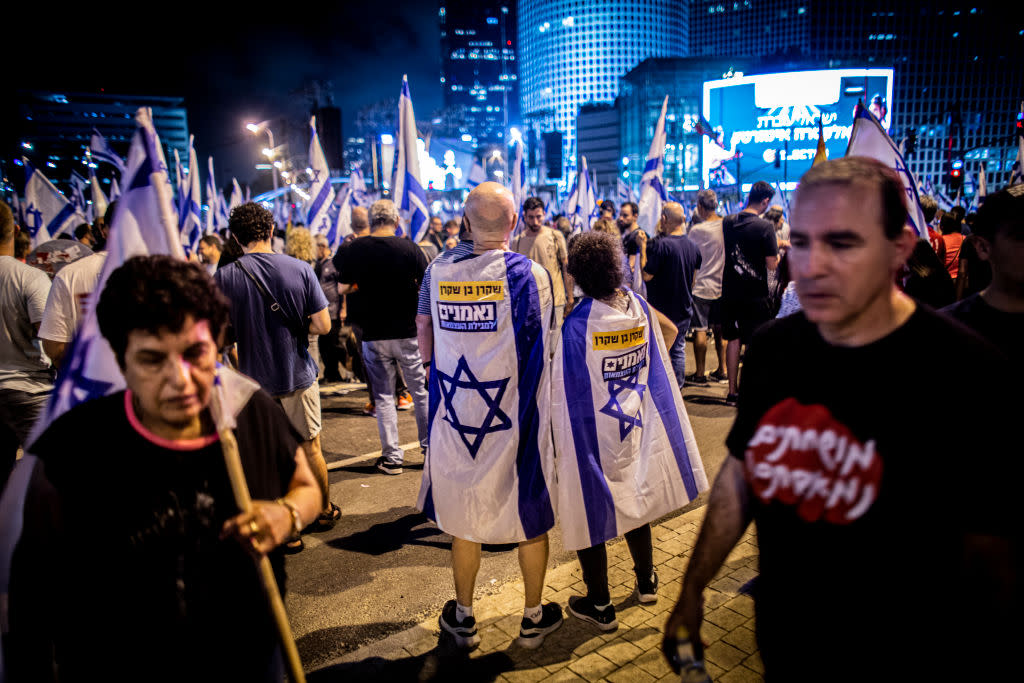 Protestors draped in the Israeli flags stand together during