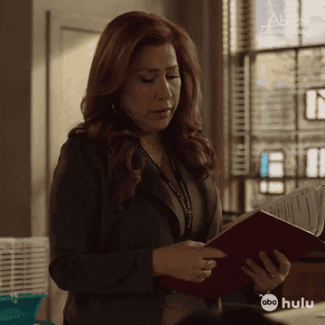 A woman examines papers in an office setting, wearing professional attire with red hair visible. Text reads: "Abbott Elementary" and "ABC Hulu."