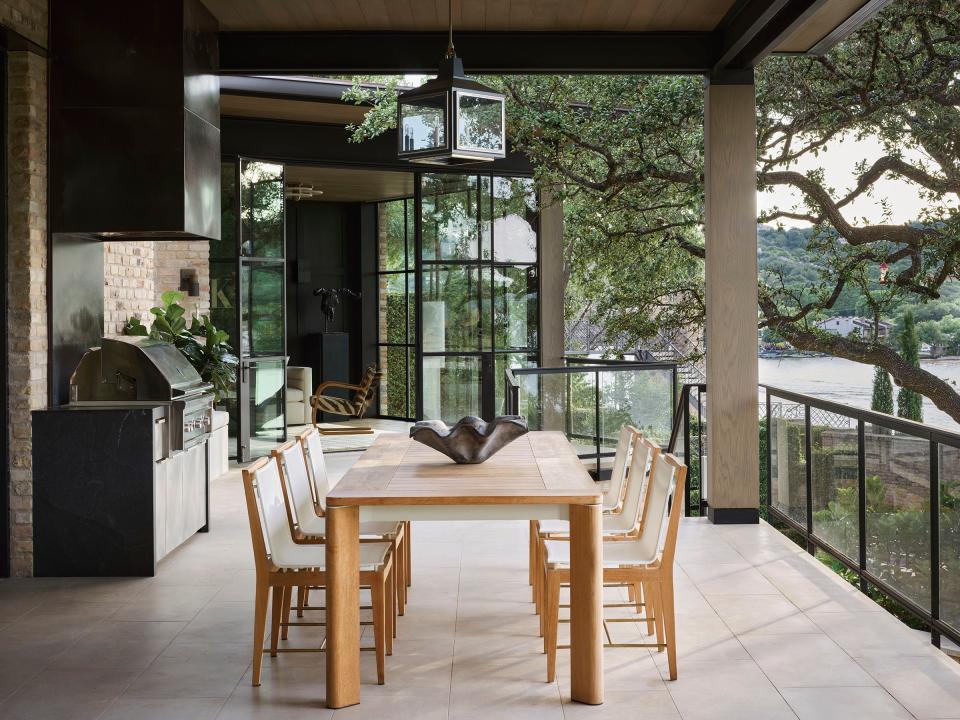 This breezy second-floor terrace overlooking the lake has a teak dining table and chairs from Harbour Outdoor. In the back we see a Wolf grill and floor-to-ceiling steel-framed glass doors. The Chelsea lantern is from The Urban Electric Company.