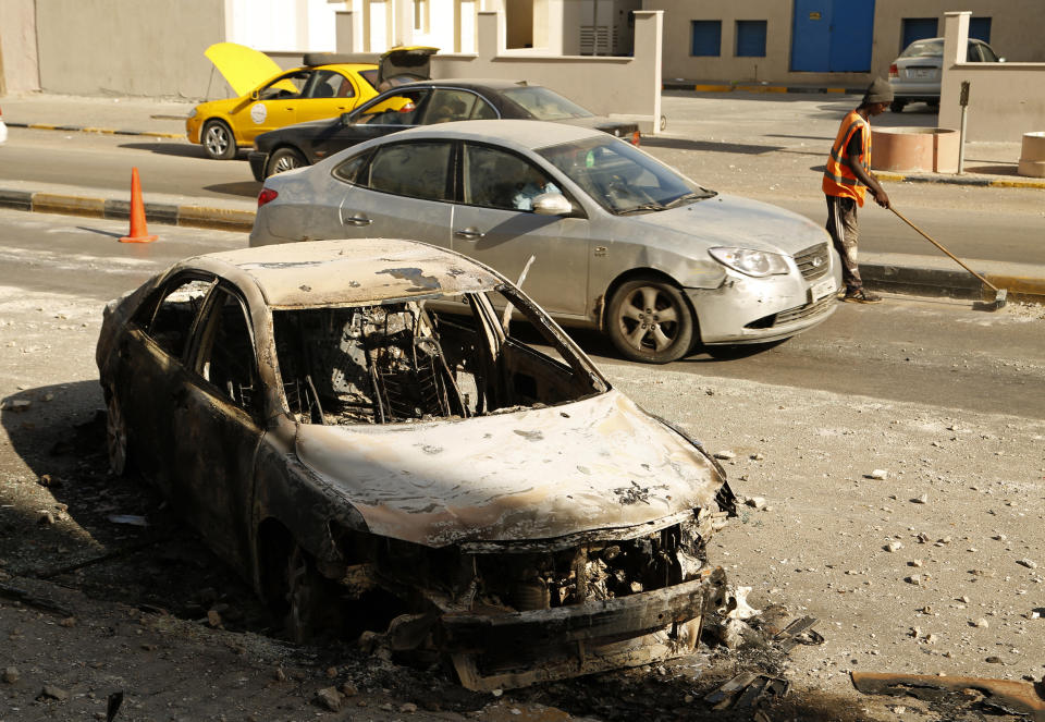 A street cleaner sweeps amid the remains of a car that was burned in clashes, in the Libyan capital of Tripoli, Sunday, August 28 2022. Deadly clashes broke out Saturday in Libya's capital between militias backed by its two rival administrations, portending a return to violence amid a long political stalemate. (AP Photo/Yousef Murad)