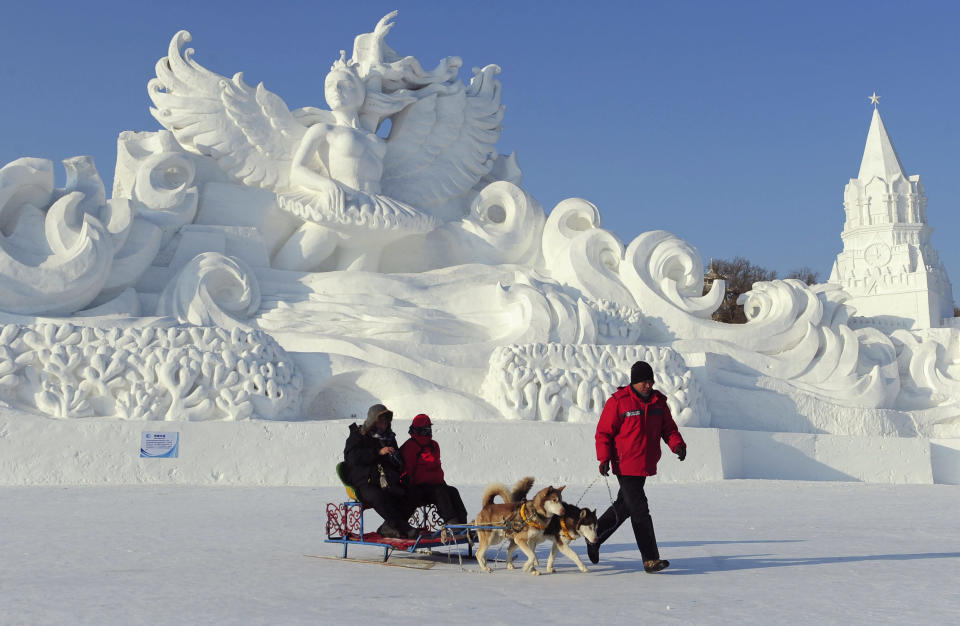 An employee pulls a dog sled carrying tourists in front of a snow sculpture ahead of the 13th Harbin Ice and Snow World in Harbin, Heilongjiang province December 26, 2011. The Harbin International Ice and Snow Festival will be officially launched on January 5, 2012. REUTERS/Sheng Li (CHINA - Tags: ENVIRONMENT SOCIETY ANIMALS TPX IMAGES OF THE DAY)