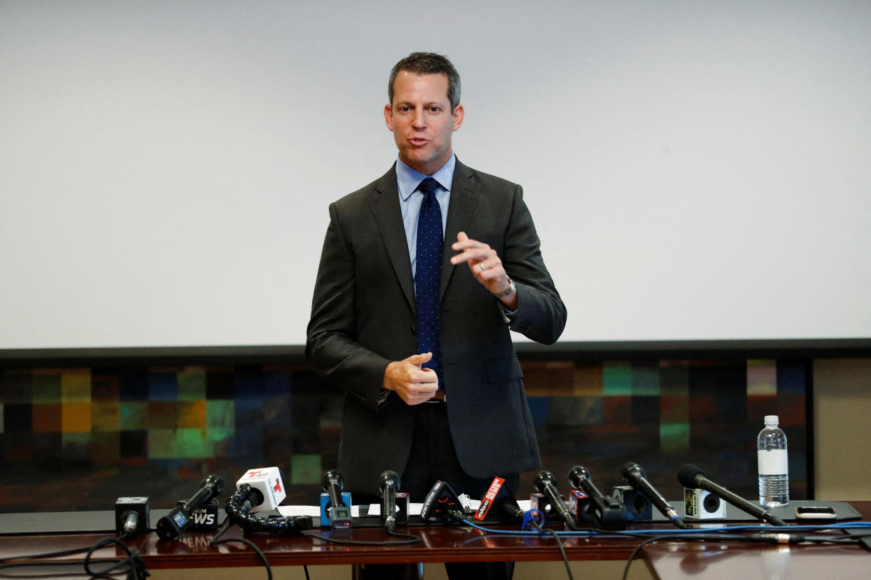 Andrew Warren speaks in front of a bank of microphones.