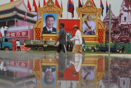 Men walk past portraits of Chinese President Xi Jinping (center, L) and Cambodian King Norodom Sihamoni ahead of his visit, in Phnom Penh, October 11, 2016. REUTERS/Samrang Pring