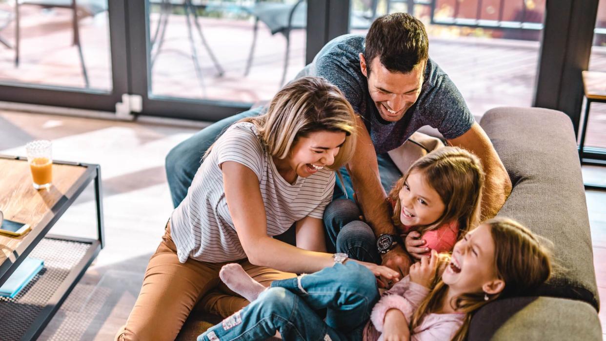 High angle view of cheerful parents having fun while tickling their daughters on sofa in the living room.