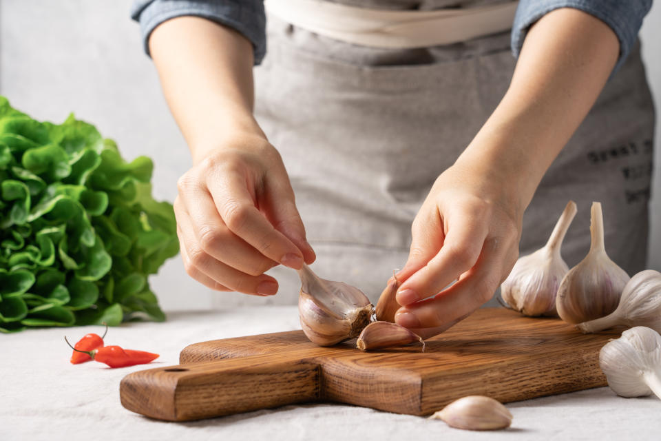 Hands peeling garlic on a wooden board with lettuce and chili peppers in the background