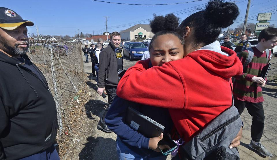 Rusty Jackson, 60, at left, watches his granddaughter Julieonna Roye, 15, center, hug his daughter and Roye's mother, Sharteya Evans, 36, at right, outside of Erie High School on April 5, 2022. Students were dismissed early after a student was shot in the leg while at school. Roye was not injured.