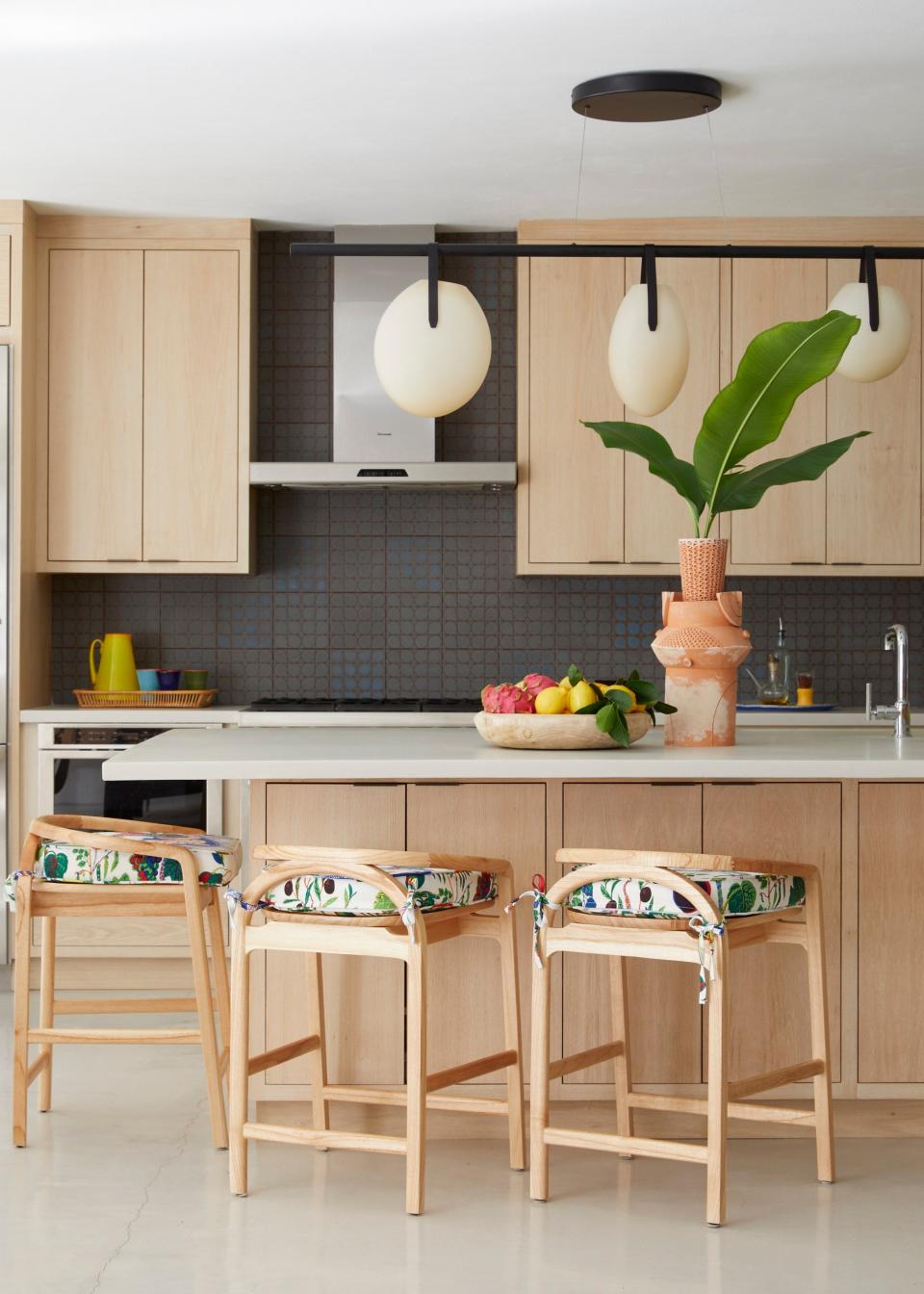 The kitchen is outfitted with white oak cabinets, Hansgrohe fixtures, and a Thermador stovetop and hood. A Rich Brilliant Willing light hangs above the concrete island surrounded by Meru counter stools from The Citizenry that have been covered in Josef Frank’s Italian Dinner fabric.