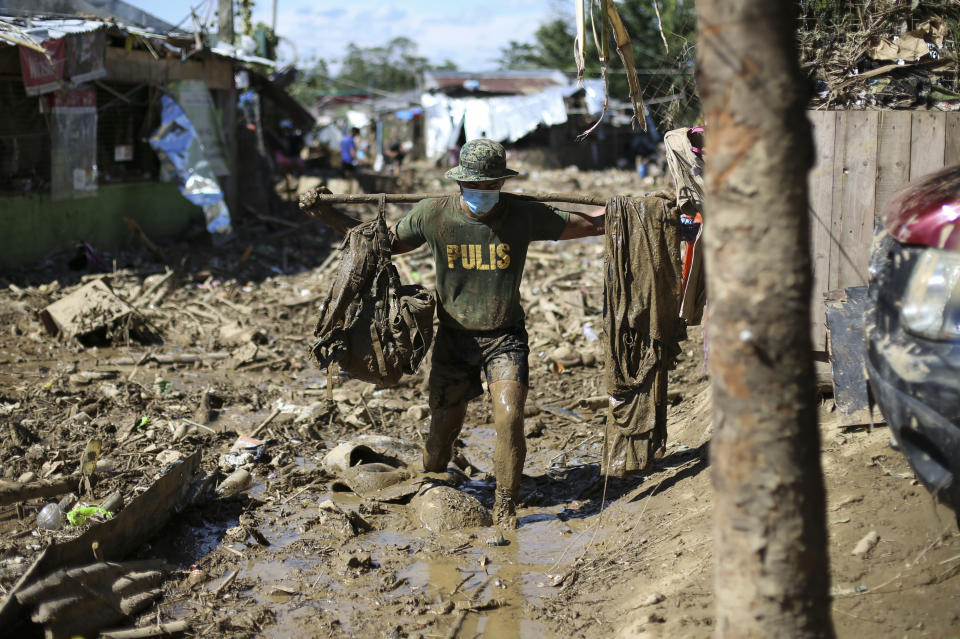 A policeman carries his belongings across debris and muds at the typhoon-damaged Kasiglahan village in Rodriguez, Rizal province, Philippines on Friday, Nov. 13, 2020. Thick mud and debris coated many villages around the Philippine capital Friday after Typhoon Vamco caused extensive flooding that sent residents fleeing to their roofs and killing dozens of people. (AP Photo/Aaron Favila)