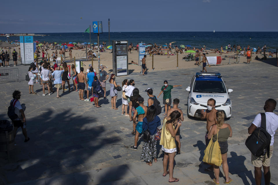 People wait to enter a beach that was closed by police due to crowding in Barcelona, Spain, Saturday, July 18, 2020. Police in Barcelona are closing access to a large area of the city's beaches due to the excess of sunbathers who decided to ignore the urgings of authorities to stay at home amid a resurgence of the coronavirus. (AP Photo/Emilio Morenatti)