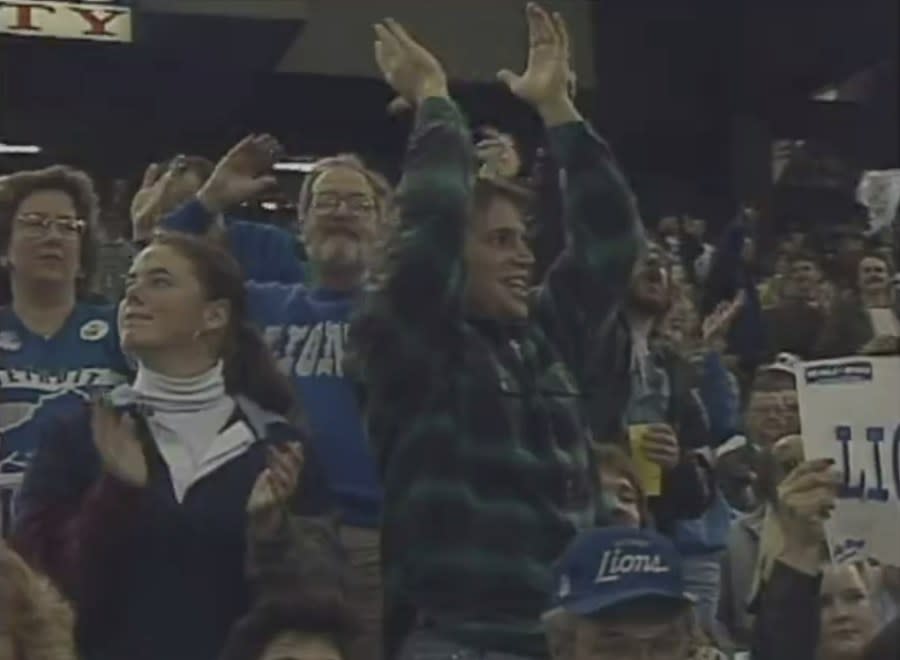 Lions fans in 1990-era clothing celebrate in the stands of the Pontiac Silverdome.