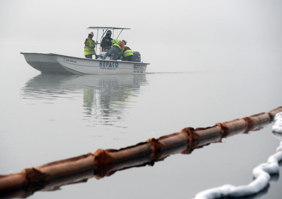 A boat motors through fog near protective boom in a creek near the Tennessee River at the scene of a fatal marina fire at Scottsboro, Ala., on Tuesday, Jan. 28, 2020. The boom was installed to contain fuel and chemicals following a dock blaze that killed several people at Jackson County Park Marina. (AP Photo/Jay Reeves)